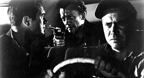 Still image of a man driving a car while the passenger in the front seat is being held at gunpoint by the man in the back seat from the film The Hitch-Hiker.