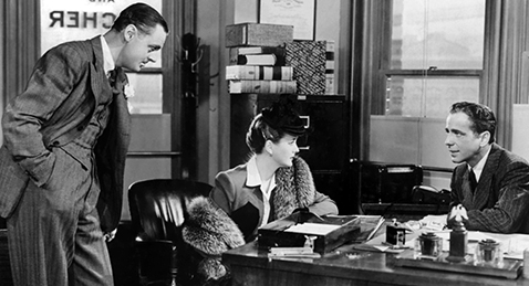 Still image of a man and women sitting at a desk while another man looks on from the film The Maltese Falcon.