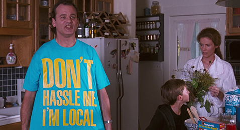 Still image of a mother and son sitting in a kitchen with Bob showing of his new shirt from the film What About Bob?