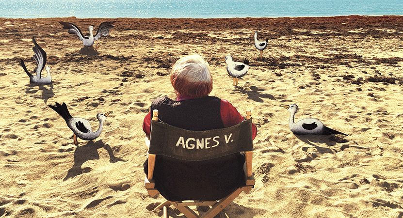 Agnès Varda sits on a beach with animated seagulls from the film Varda by Agnès