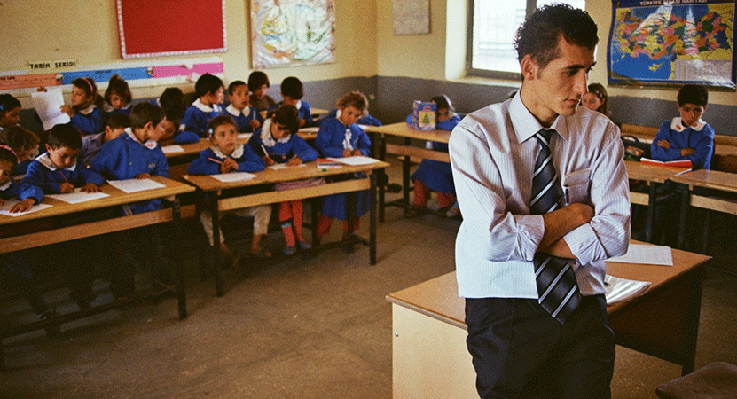 a man stands with his back to a classroom fill of kids from the film  İki Dil, Bir Bavul (On the Way to School)